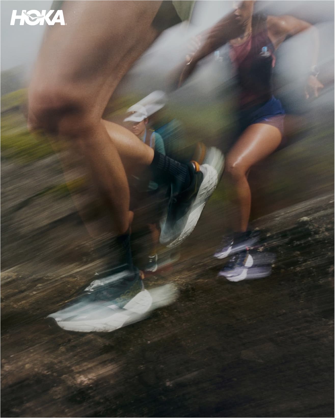 Blurred image of runners mid-stride on a trail, highlighting movement and speed. HOKA logo in the top left corner.