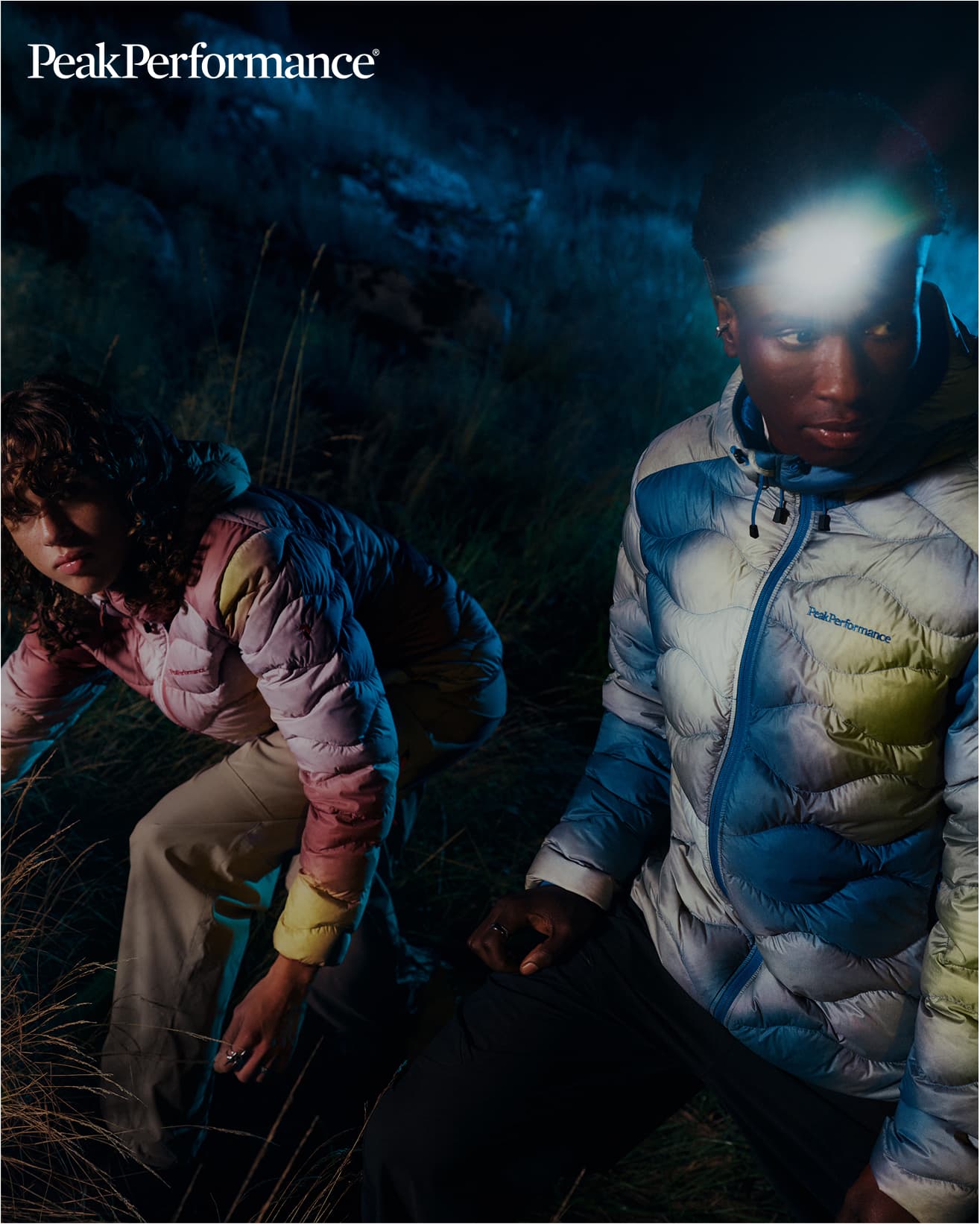 Two people in colorful puffer jackets outdoors at night, one wearing a headlamp. With Peak Performance branding in the corner.