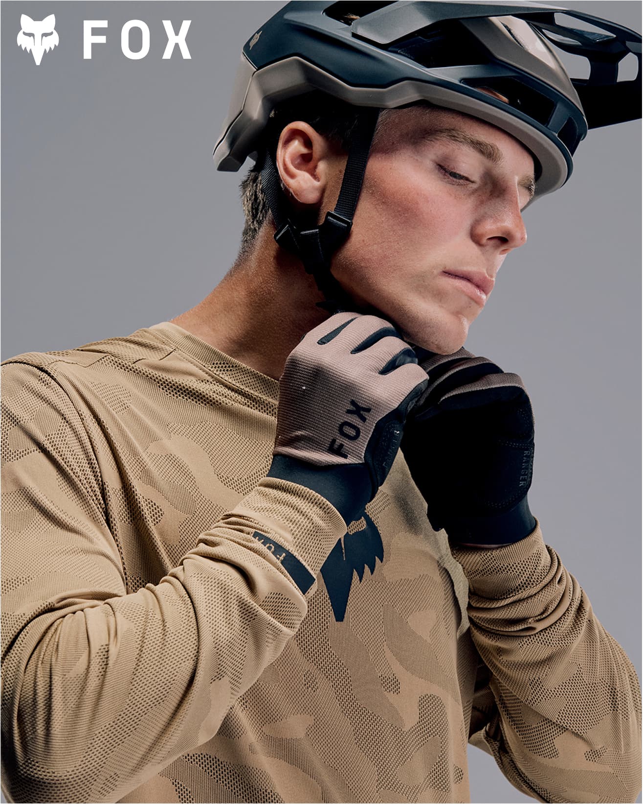 Person wearing a helmet and gloves secures the chin strap of their helmet. With Fox branding in the corner.