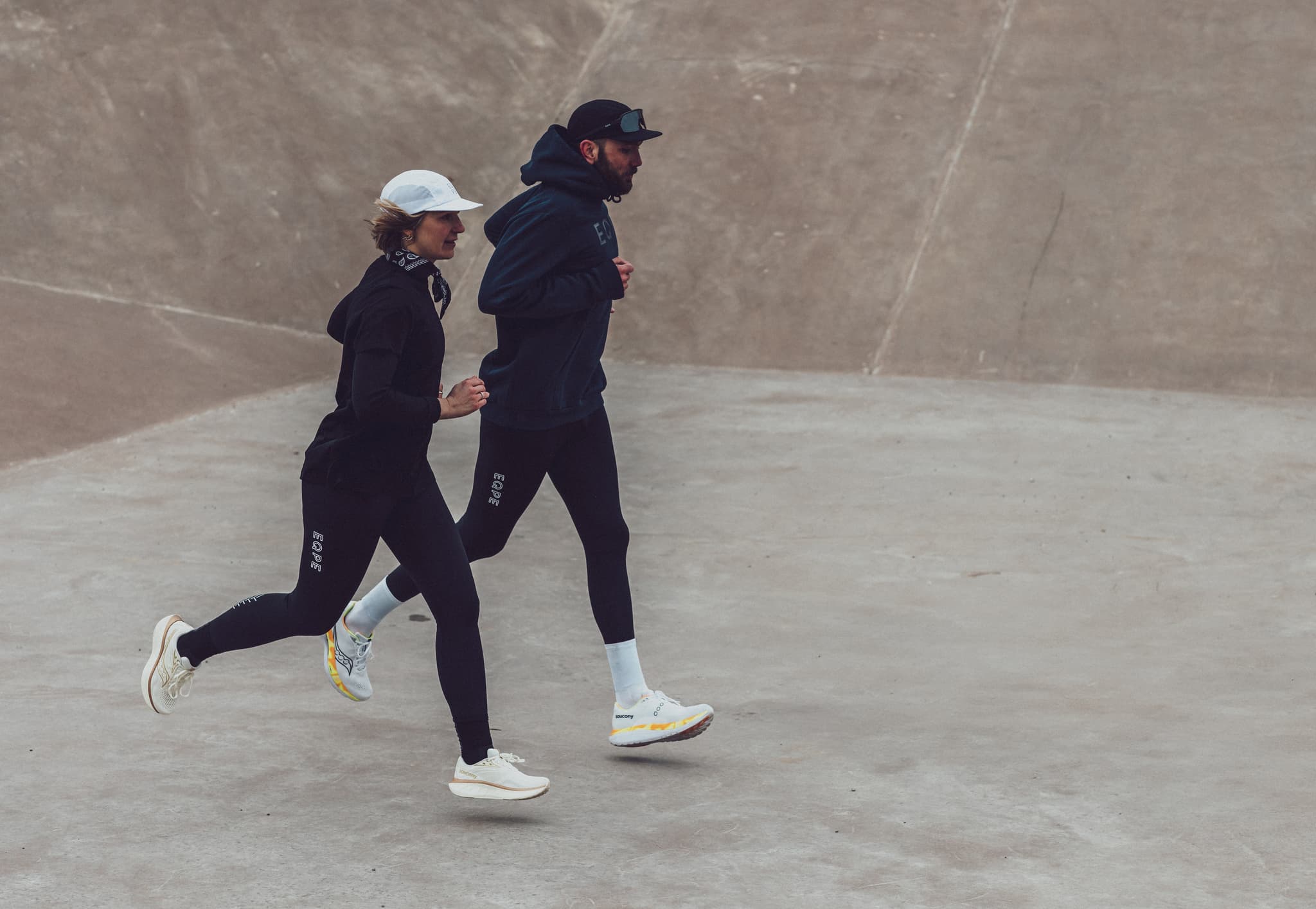 Two people in athletic wear jogging together on a concrete surface.